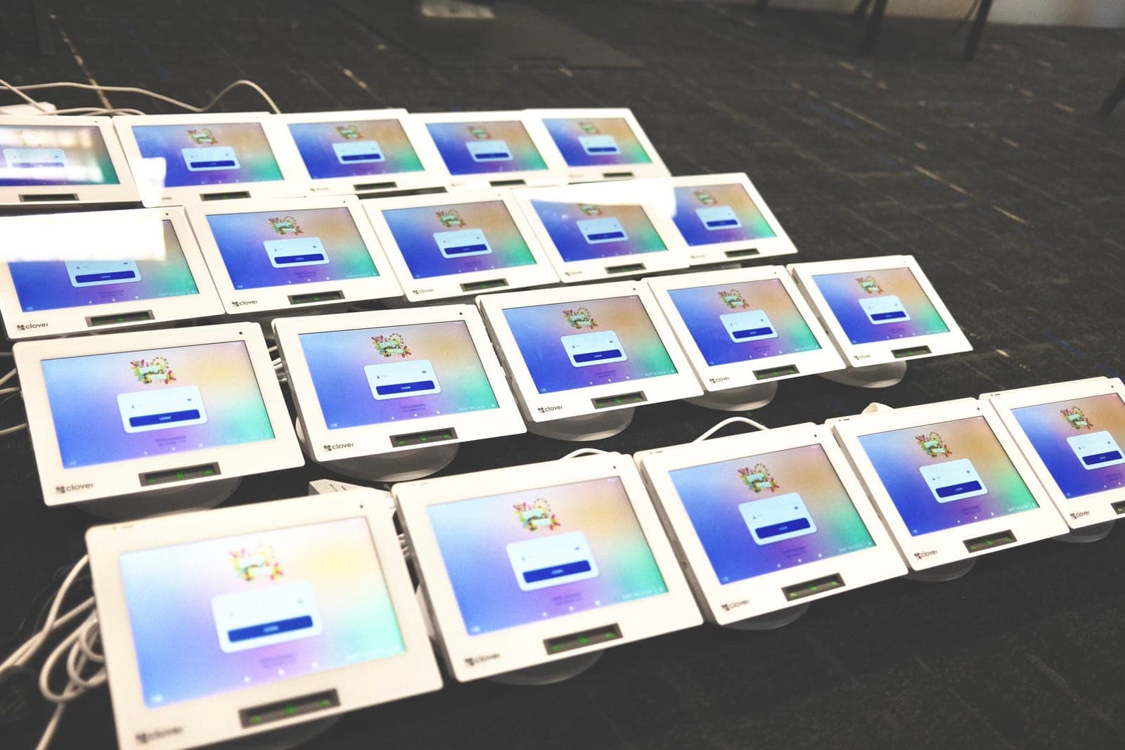 A pre-event fleet of Clover Mini terminals on a charging table, all on the Carnival Fun Pass login screen, ready to deploy