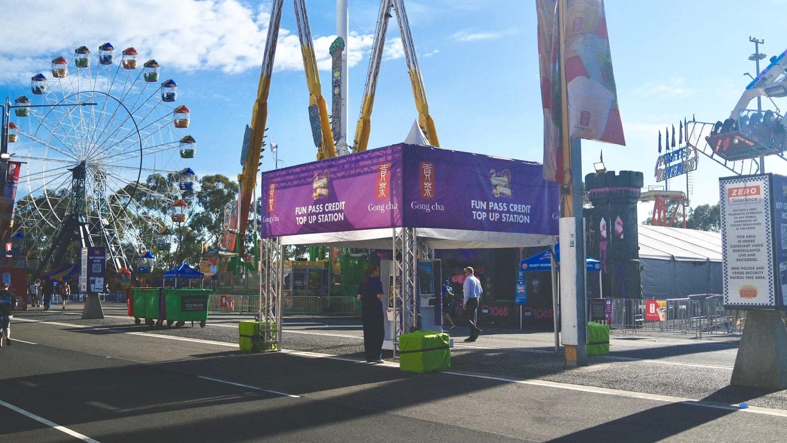 Far view of the Fun Pass Credit Top Up Station tent at the Sydney Royal Easter Show, with the Ferris wheel and Gong Cha banners surrounding the palletised pavilion